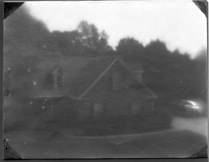 The same image that my camera got but the contrast is greatly enhanced. There is a house in front of the trees with a parked car to the right.